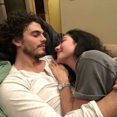 a man and woman laying on a bed together, one is kissing the other's forehead