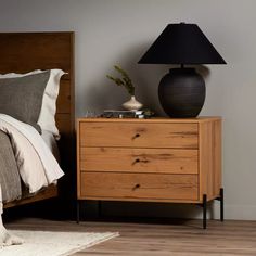 a nightstand with a lamp on top of it next to a bed