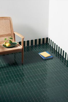 a chair sitting next to a bowl of fruit on top of a green tiled floor