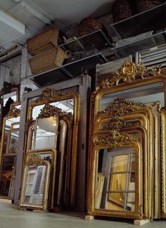 several gold framed mirrors sitting on the floor in front of a storefront window with shutters open