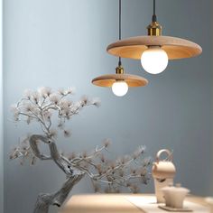 three lights hanging from the ceiling above a table with a vase and teapot on it