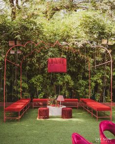 an outdoor seating area is set up with red cushions and pink umbrellas, surrounded by greenery