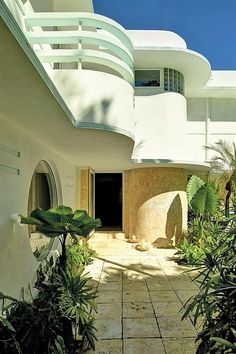 an entrance to a white building surrounded by trees and plants