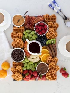 a platter filled with waffles, fruit, and other foods next to two cups of coffee