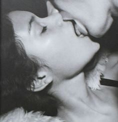 black and white photograph of a man kissing a woman's face with feathers on her nose