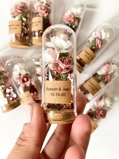 a person holding a tiny bottle filled with flowers and sand in front of other small bottles