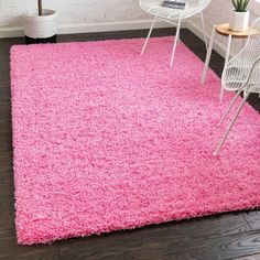 a bright pink rug in the corner of a room with white chairs and a potted plant