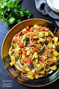 a bowl filled with pasta and veggies on top of a table next to some parsley