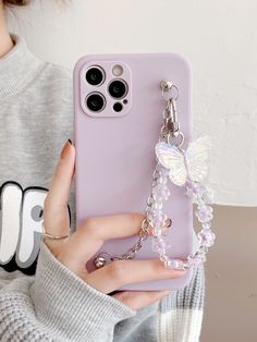 a woman holding up her phone case with a butterfly charm attached to the back of it