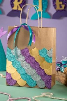 a paper bag that has mermaid scales on it and a purple ribbon around the handle