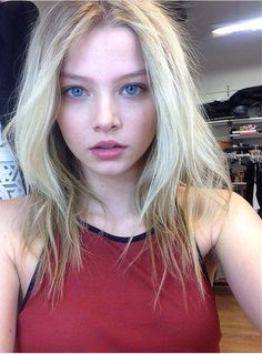 a woman with blonde hair and blue eyes in a red tank top looking at the camera