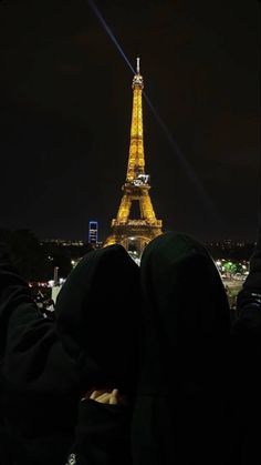 two people sitting in front of the eiffel tower at night with their feet up