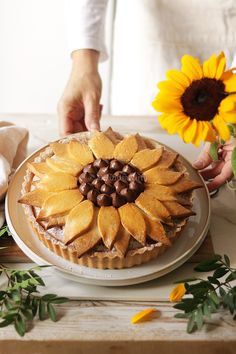 a person decorating a cake with chocolate and sunflowers on the table next to it