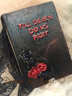 a book that has been decorated with roses and writing on the cover is sitting on a lace tablecloth