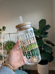 a person holding a glass cup with the words mama on it in front of a potted plant