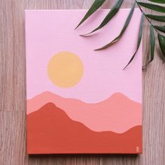 an orange and pink painting sitting on top of a wooden table next to a plant