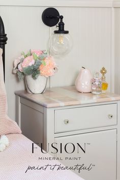 a white dresser sitting next to a bed with pink flowers on it and a light fixture