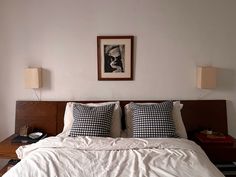 a bed with white sheets and black checkered pillows in a small room next to a painting on the wall