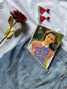 a book sitting in the back pocket of a pair of jean shorts next to a red rose