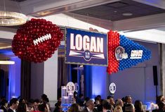 people are sitting at tables with balloons and footballs hanging from the ceiling in front of them