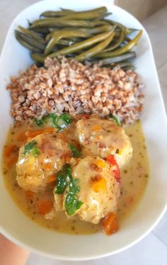 a white plate topped with green beans, rice and meat covered in gravy