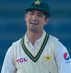 a man wearing a green hat and white sweater smiles while standing in front of a blue wall