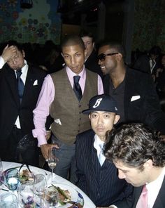 a group of men standing around a table with wine glasses on it and one man wearing a hat