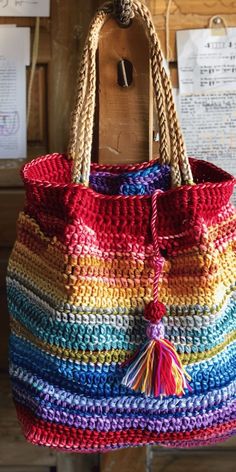 a multicolored crocheted bag hanging from a wooden hook on a wall