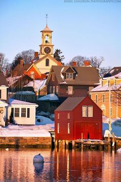 a red house sitting on top of a lake next to snow covered ground and houses