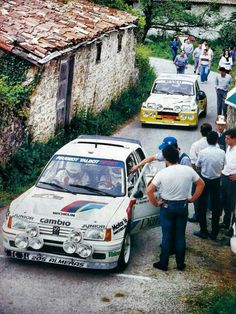 several people standing around cars parked on the side of a road