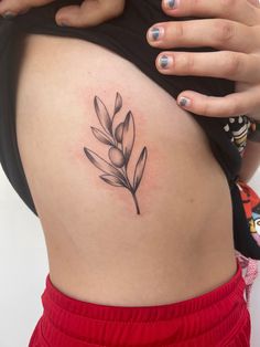 a woman's stomach with a small leaf tattoo on the side of her belly