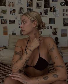 a woman with tattoos on her arm sitting in front of a wall full of pictures