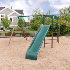 a green slide in the sand at a park with houses in the backround