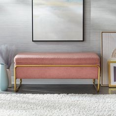 a pink bench sitting on top of a white rug next to a painting and vase