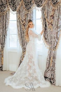 a woman standing in front of a window wearing a wedding dress with long sleeves and sheer lace