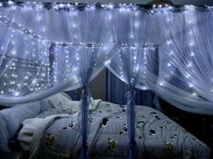 a canopy bed with white curtains and fairy lights