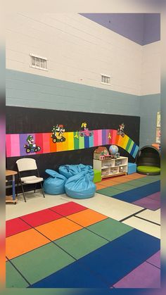 an indoor play area with rainbow colored tiles and toys on the floor, including bean bag chairs