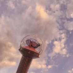 a glass ball sitting on top of a metal pole under a cloudy sky with clouds