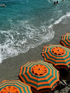 several orange and green umbrellas sitting on the beach next to the ocean with people swimming in the water