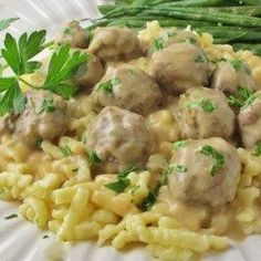 a white plate topped with pasta and meatballs covered in gravy next to asparagus