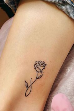 a small rose tattoo on the side of a woman's leg, it is black and white