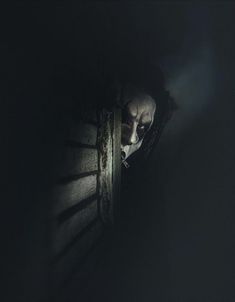 a creepy looking person peeking out from behind a wooden fence in the dark with his head down