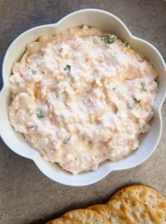 a white bowl filled with dip next to crackers on top of a gray surface