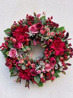 a wreath with red flowers and greenery hanging on the wall in front of a white wall