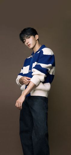 a young man standing in front of a brown background wearing a blue and white sweater