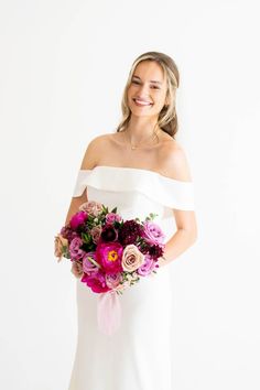 a woman in a white dress holding a bouquet of pink and purple flowers on her wedding day