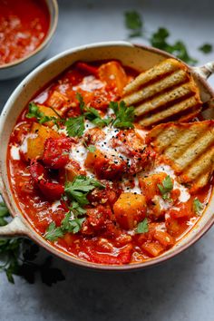 a bowl filled with tomato soup and grilled bread