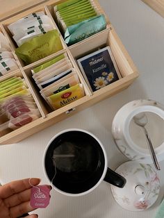 a person holding a coffee cup next to a drawer with tea bags and other items in it