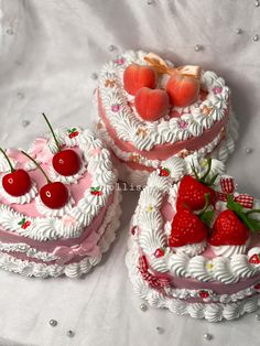 three heart shaped cakes with cherries and strawberries on top are sitting on a white tablecloth