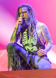 a man with long hair and tattoos sitting on a stage